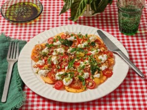 Peach & Tomato Caprese with Ricotta on a plate with a red and white checkered tablecloth