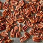 Roasted pecan halves scattered on a metal baking tray.