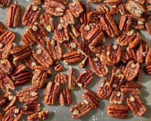 Roasted pecan halves scattered on a metal baking tray.